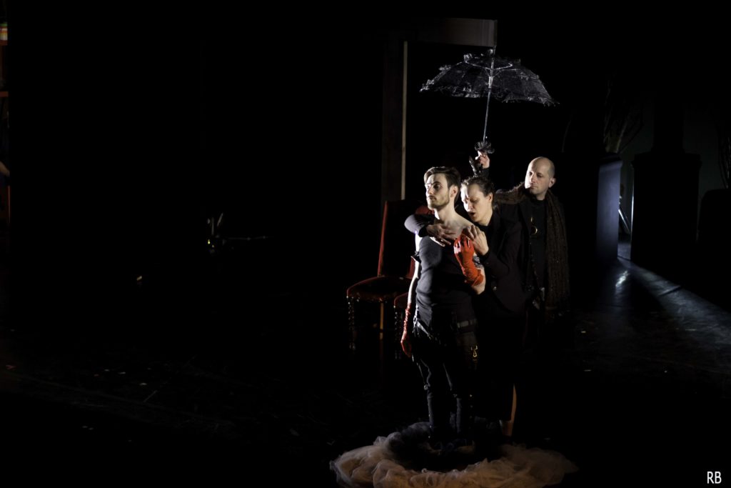 Trois personnages sont sous une ombrelle.